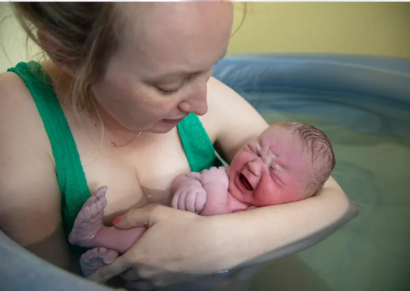 Mutter hält ihr eben geborenes Baby im warmen Wasser der Gebärwanne an der Brust