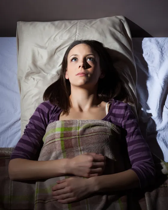 Schwangere liegt wach auf dem Bett, in eine Decke gehüllt, und schaut zur Decke